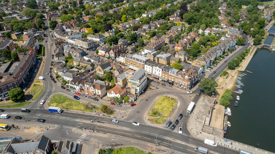 An aerial view of Ruislip High Street in the HA4 area, showcasing a mix of residential and commercial buildings with narrow streets and parked cars. To the right, there is a river with several boats m