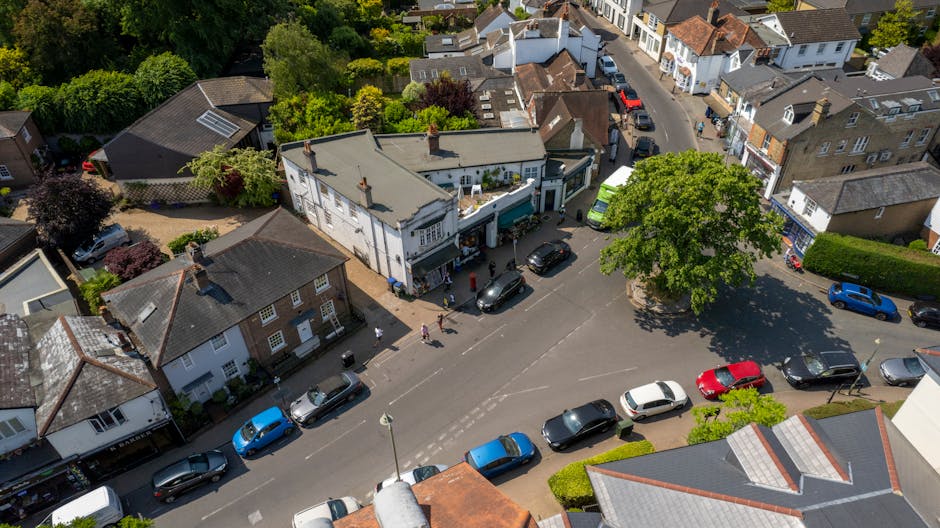 An aerial view of Ruislip High Street in the HA4 area, showcasing a mix of residential and commercial buildings with narrow streets and parked cars. To the right, there is a river with several boats m